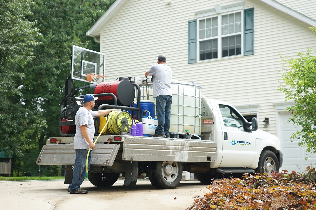 employees preparing pressure washing equipment outside a home